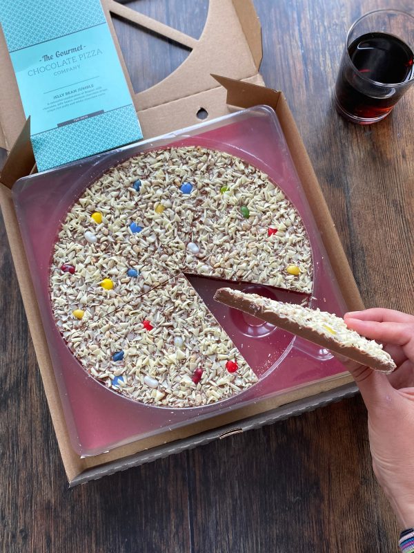 10" Jelly Bean Jumble chocolate pizza with a piece in out in someones hand